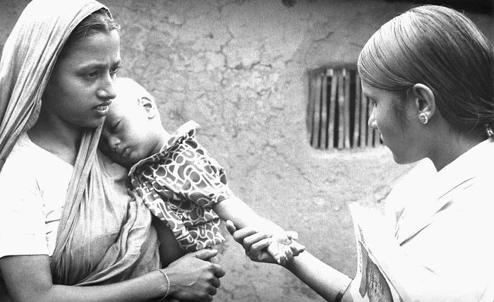 This volunteer smallpox eradication team vaccinator (right) was in the process of checking the smallpox vaccination scar on this young child's left forearm, while he rested his head upon his mother's shoulder